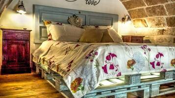 A rustic bedroom with a wooden bed frame, floral bedding, and a curved stone wall.