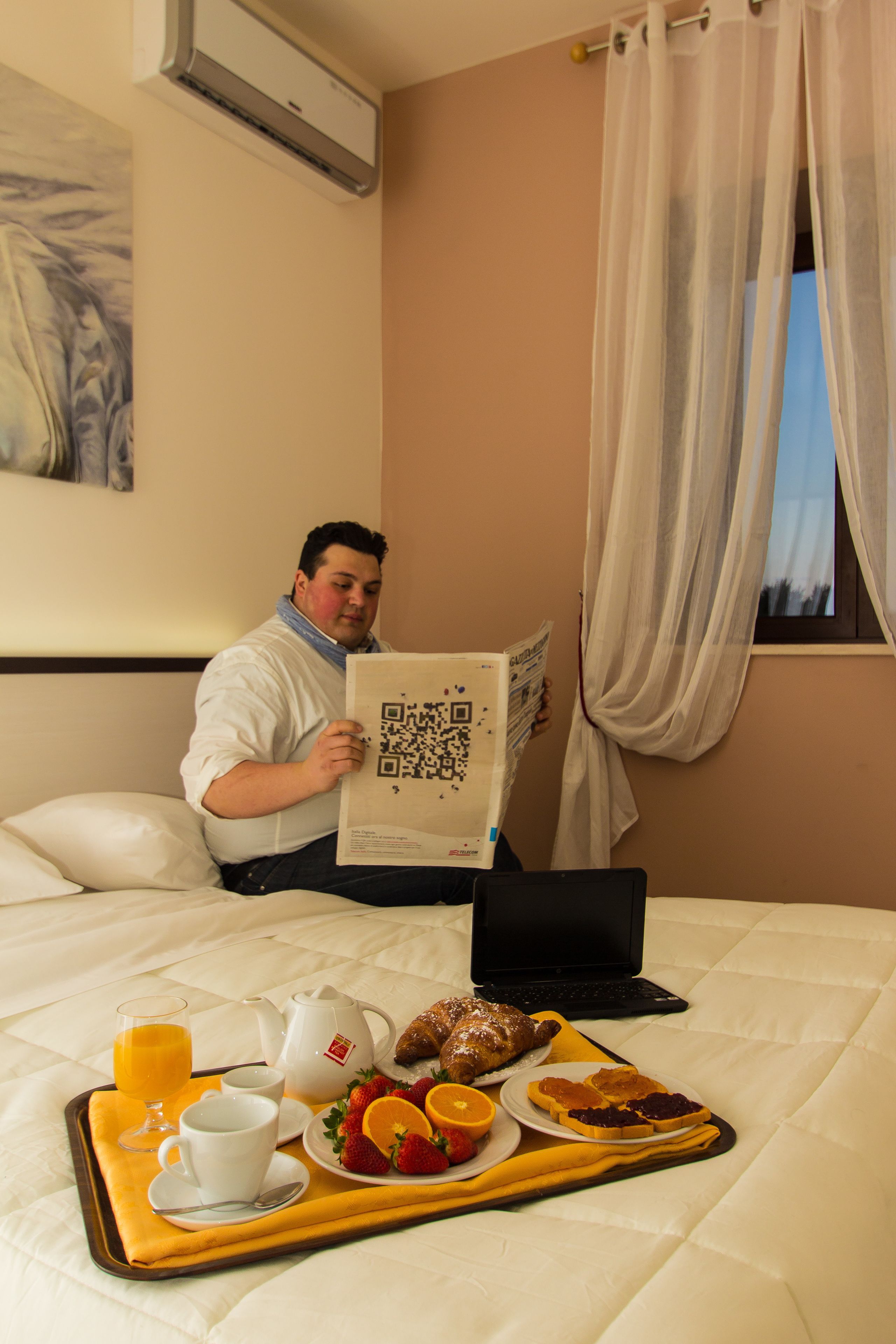 A hotel room with a bed, a tray with breakfast items, a laptop, and a window with curtains.