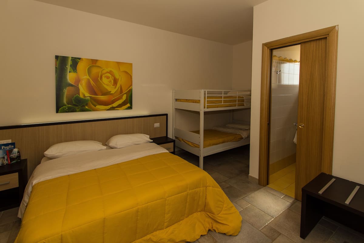 A room with a bed, bunk beds, a painting, a nightstand, and a door.