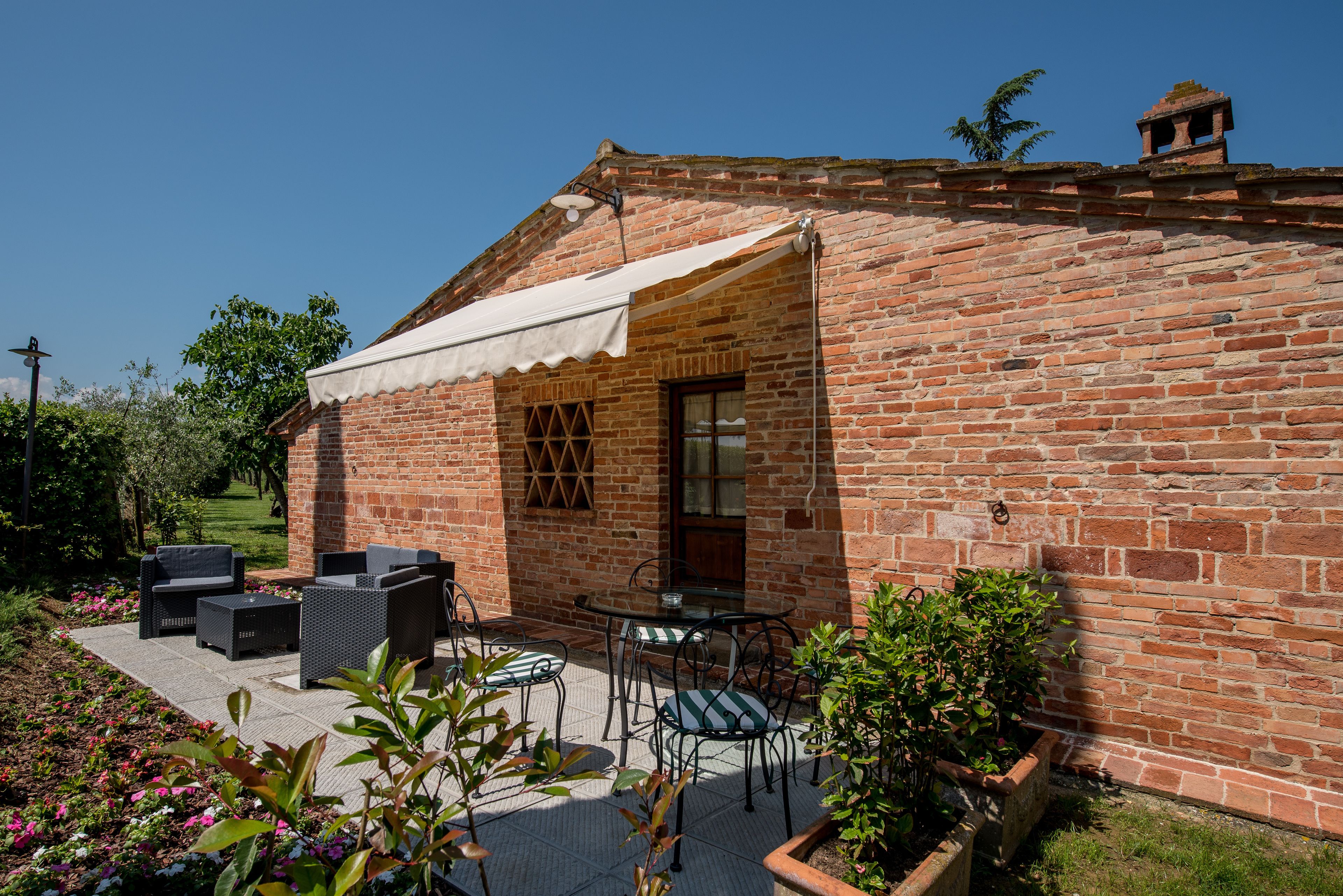 Un bâtiment en briques doté d’un patio couvert, aménagé avec du mobilier d’extérieur et un jardin.
