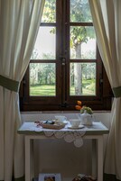 Una ventana con vistas a un paisaje verde, una mesa con un calentador de agua, tazas y una bandeja de bocadillos.