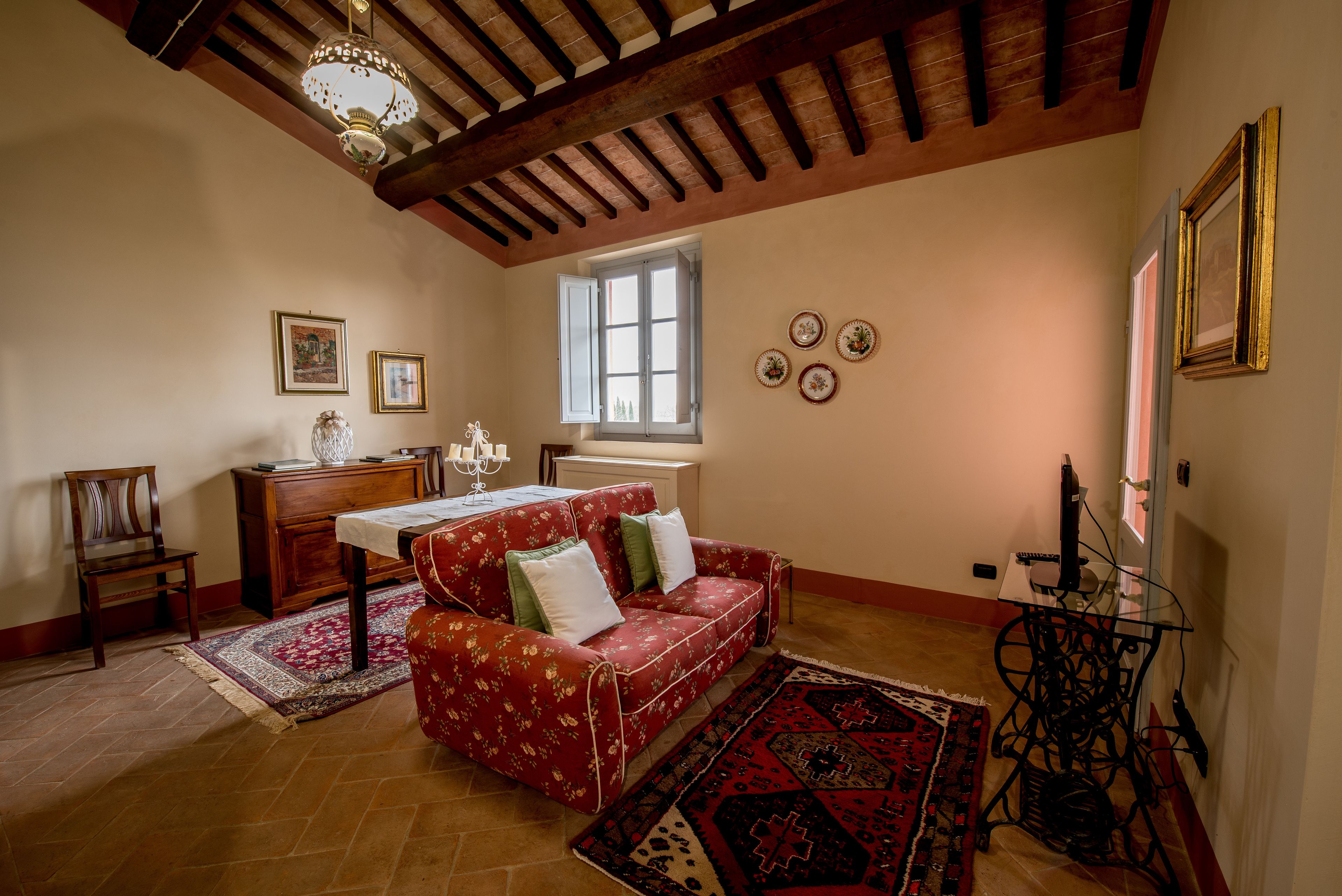 Ein gemütliches Zimmer mit einem roten Sofa, Holzmöbeln, einer Kristallleuchtre und einem Fenster mit Blick.
