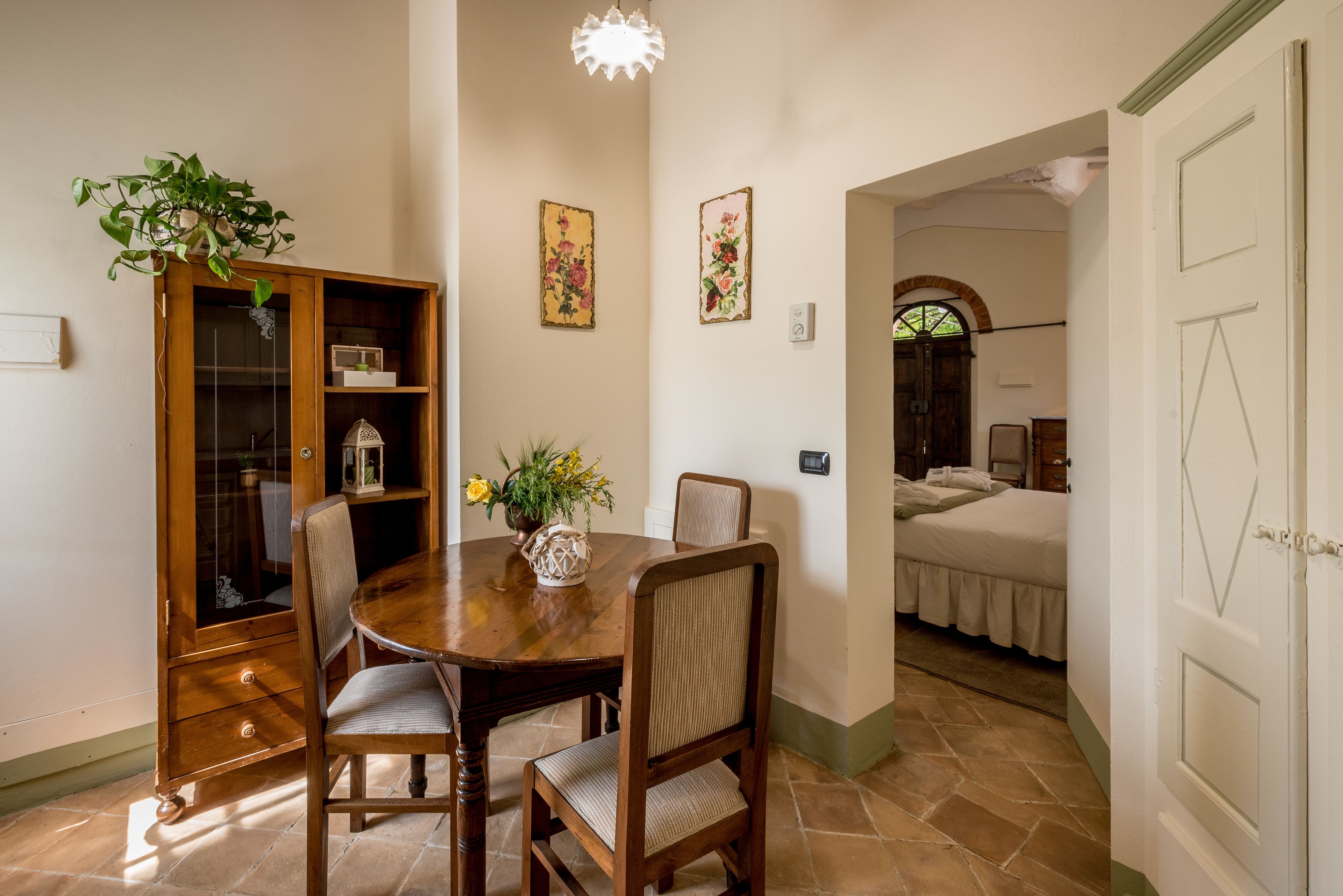 A dining area with a wooden table and chairs, a cabinet with glass doors, and two floral wall decorations.