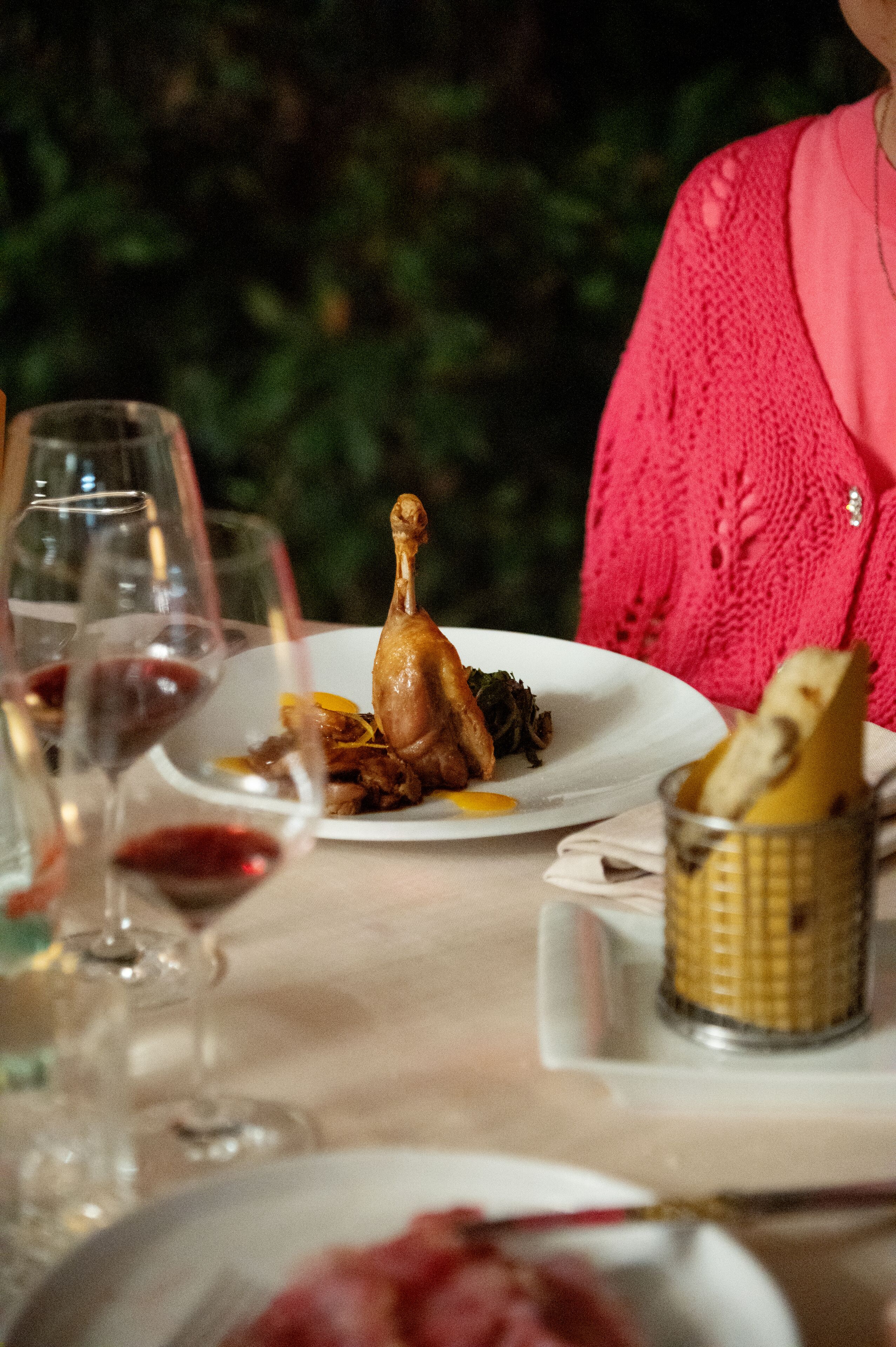 A dining table with plates of food, wine glasses, and a basket of bread.