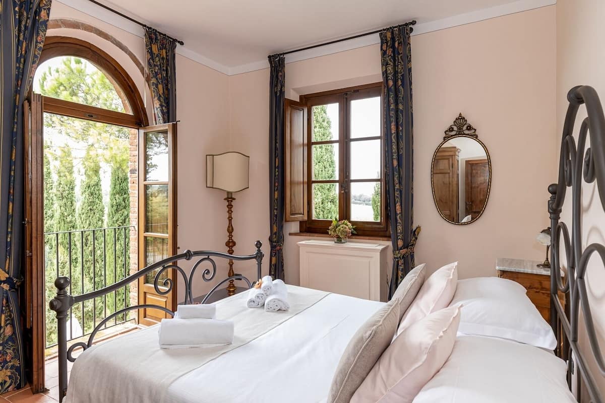 A bedroom with a bed, a window, a mirror, and a view of greenery outside.