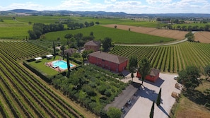 An aerial view of a vineyard estate with rows of grapevines, a swimming pool, and a red building. - Podere La Rocca (Montepulciano)