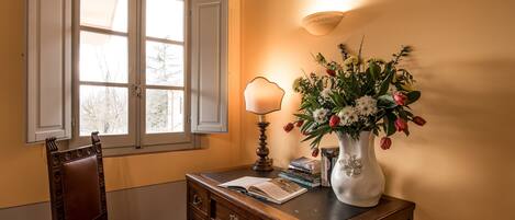 A wooden desk with a vase of flowers, a lamp, and books.