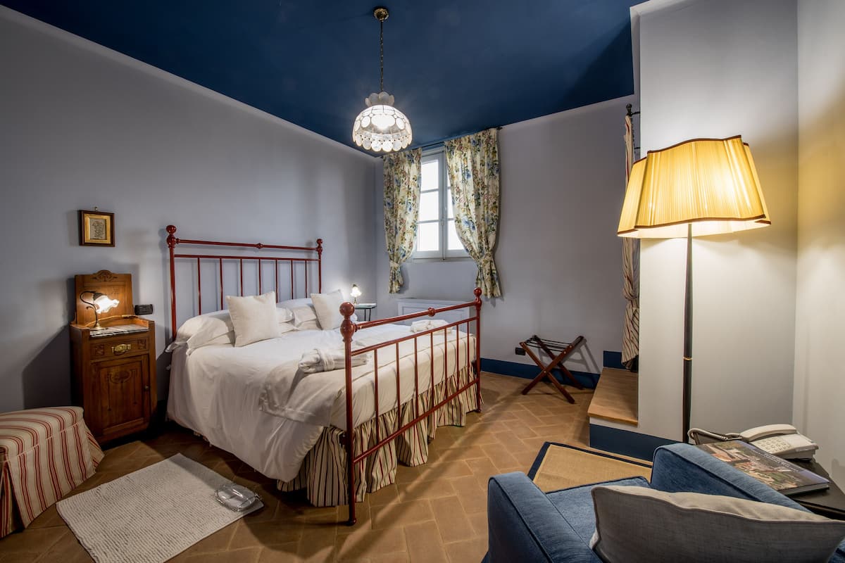 A bedroom with a bed, a nightstand, a lamp, a chair, and a window with curtains.