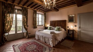 A bedroom with a large bed, wooden headboard, a chandelier, a nightstand, and a red rug. - Podere La Rocca (Montepulciano)