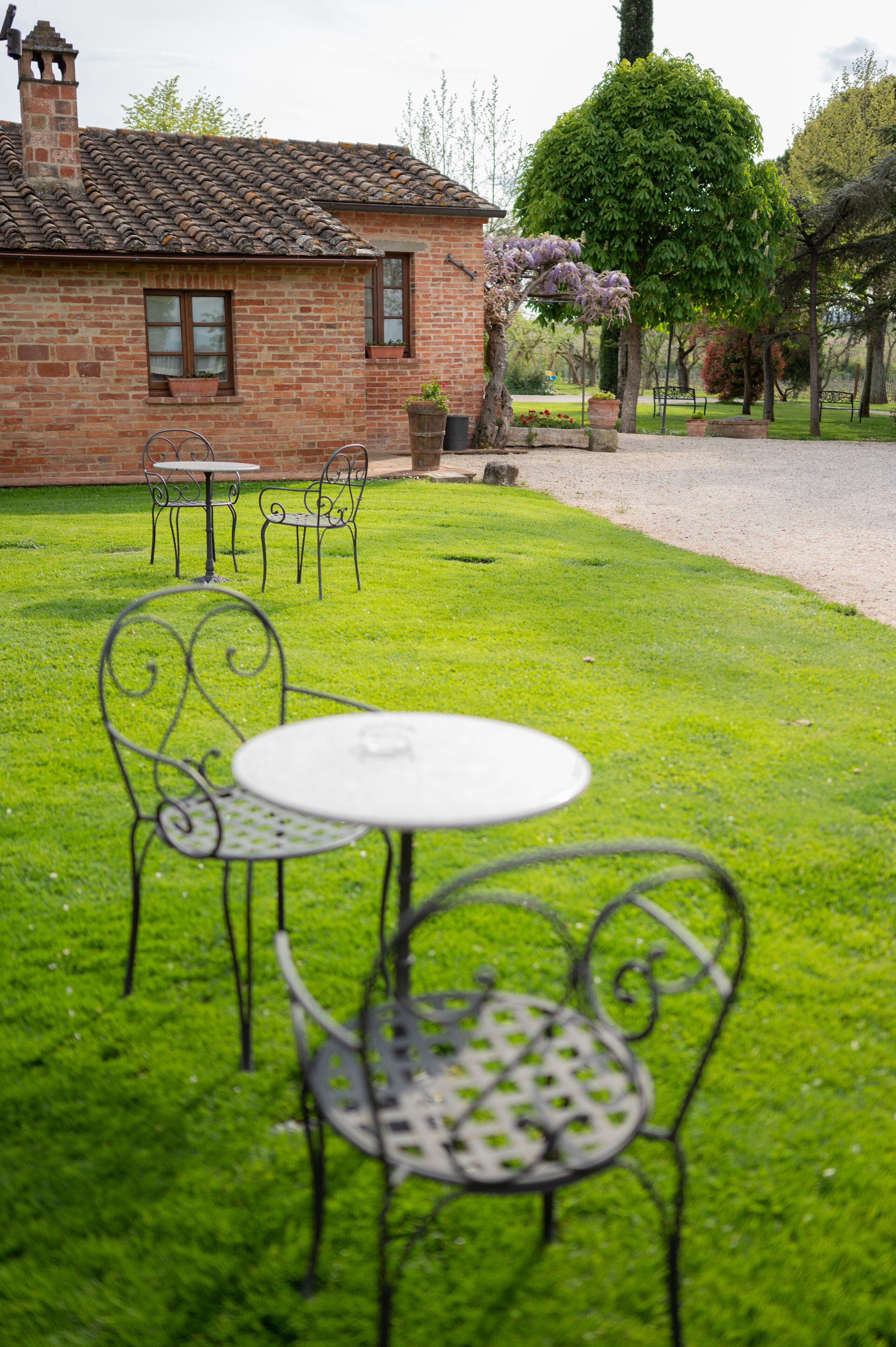 A brick house with a tiled roof, a lawn, and metal chairs and tables.