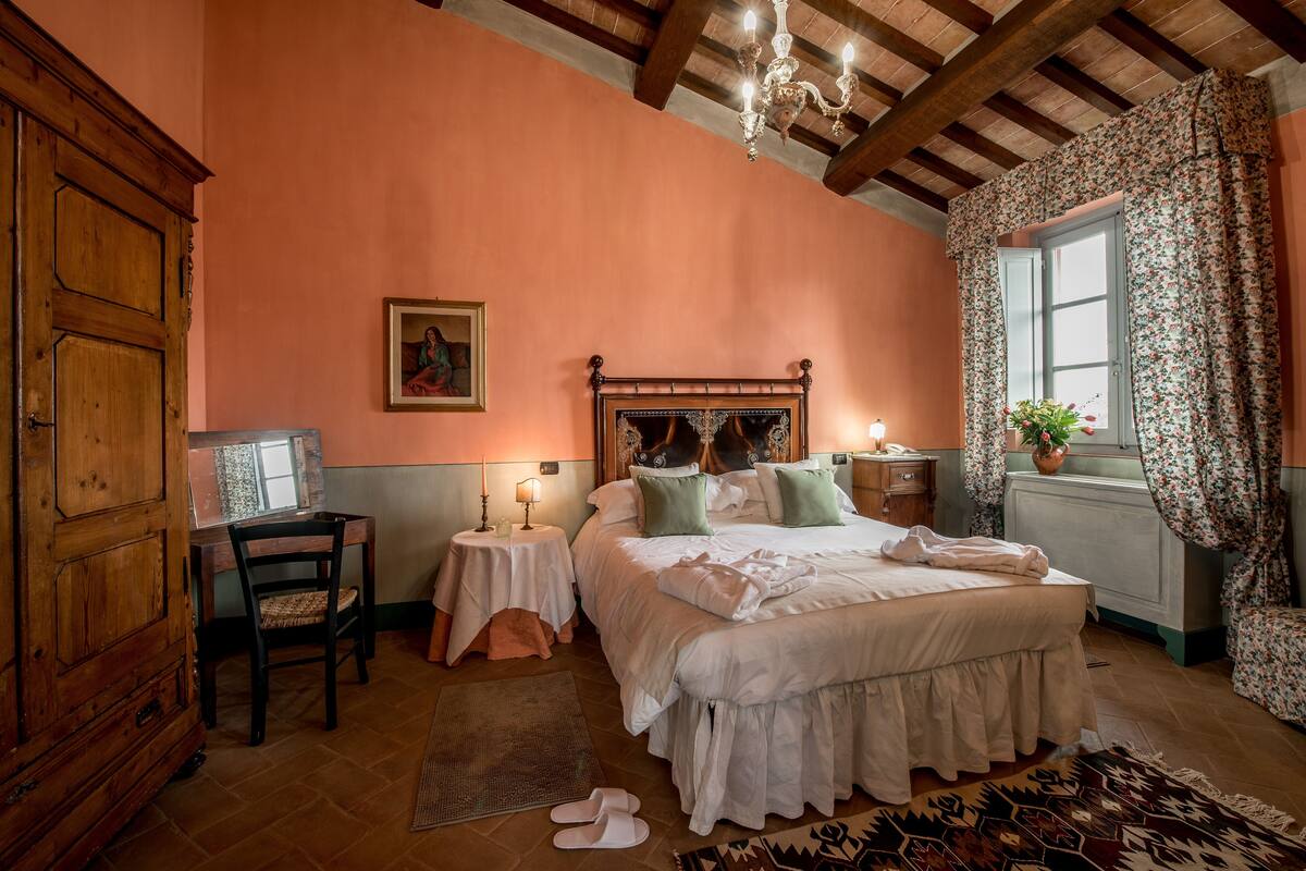 A bedroom with a wooden bed, a nightstand, a chair, a desk, and a window with curtains.
