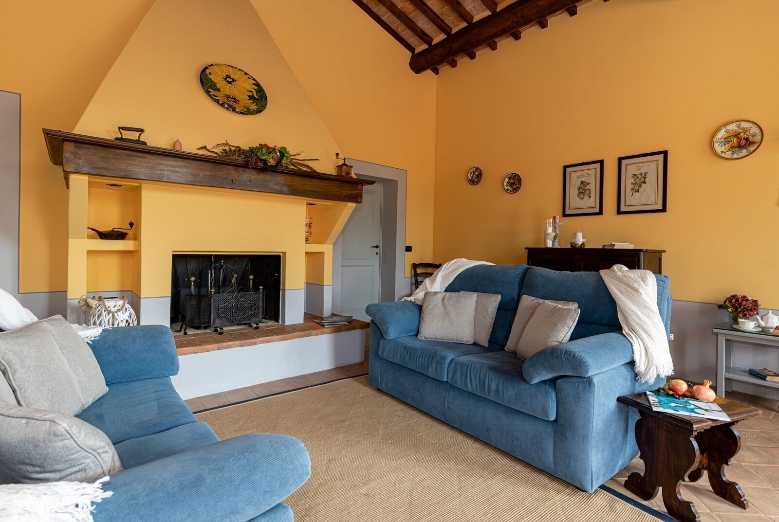 Una sala de estar con chimenea, sofá azul y pared amarilla.