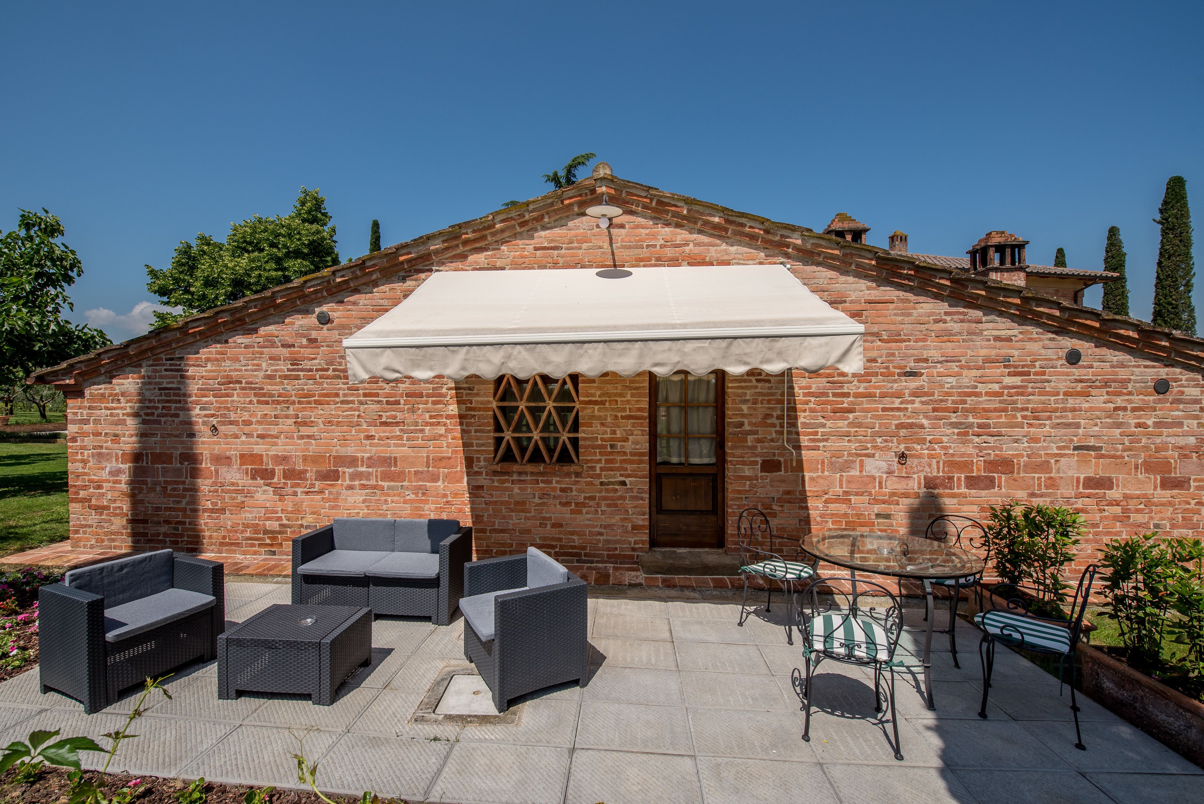 A brick building with a covered patio area featuring outdoor furniture and a table.