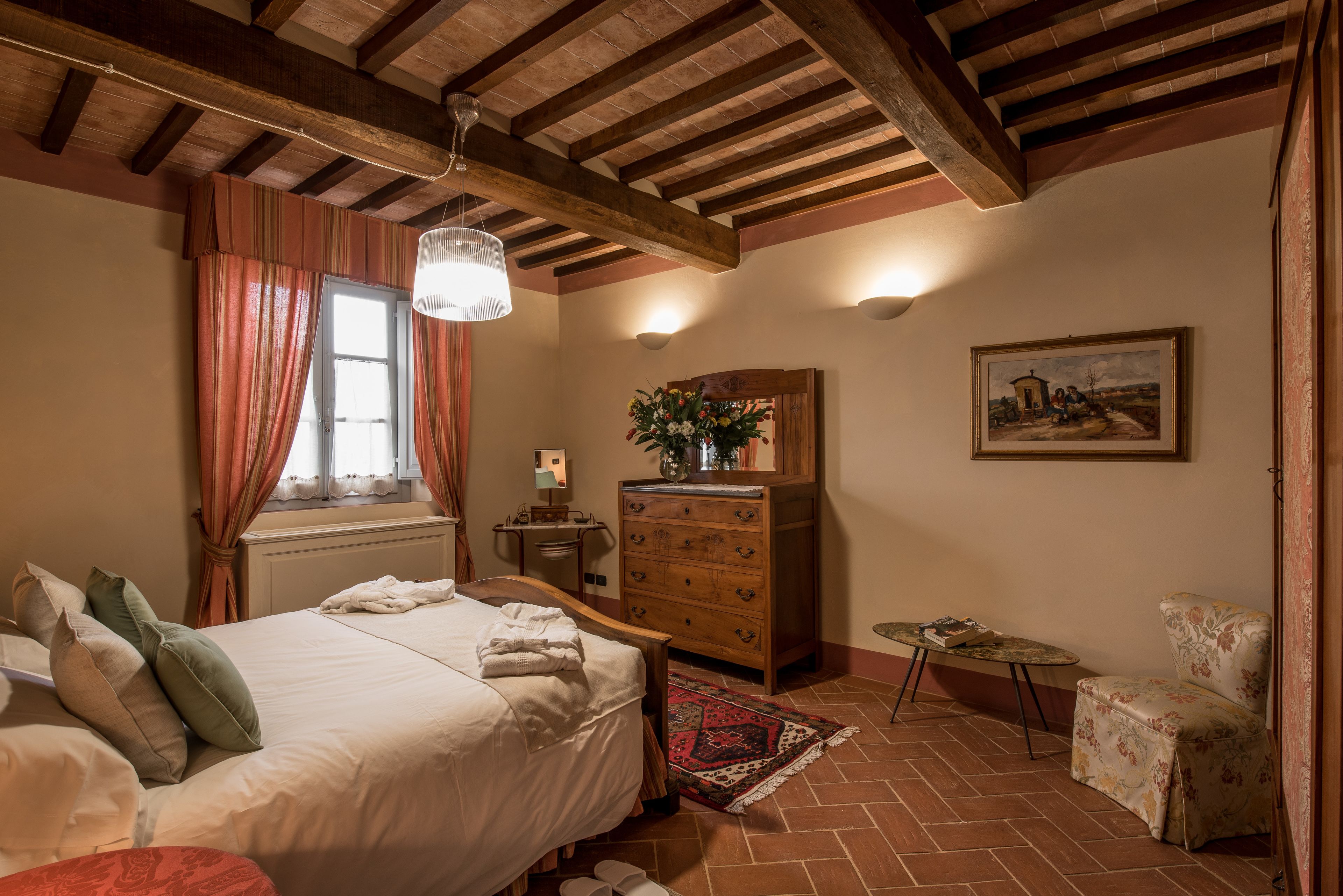 Un dormitorio con una cama grande, vigas de techo de madera, un aparador, una silla y un cuadro en la pared.