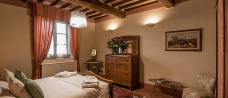 Un dormitorio con una cama grande, vigas de techo de madera, un aparador, una silla y un cuadro en la pared.