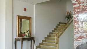 A staircase with a golden handrail and a wooden console table with a mirror and flowers. - Hotel Quisisana (Chianciano Terme)
