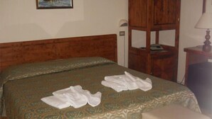 A hotel room with a wooden headboard, a patterned bedspread, two white towels on the bed, and a small bedside table with a lamp. - Hotel Quisisana (Chianciano Terme)