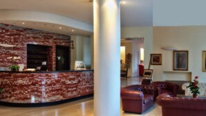 A lobby with a marble reception desk, leather sofas, and a fireplace. - Hotel Quisisana (Chianciano Terme)