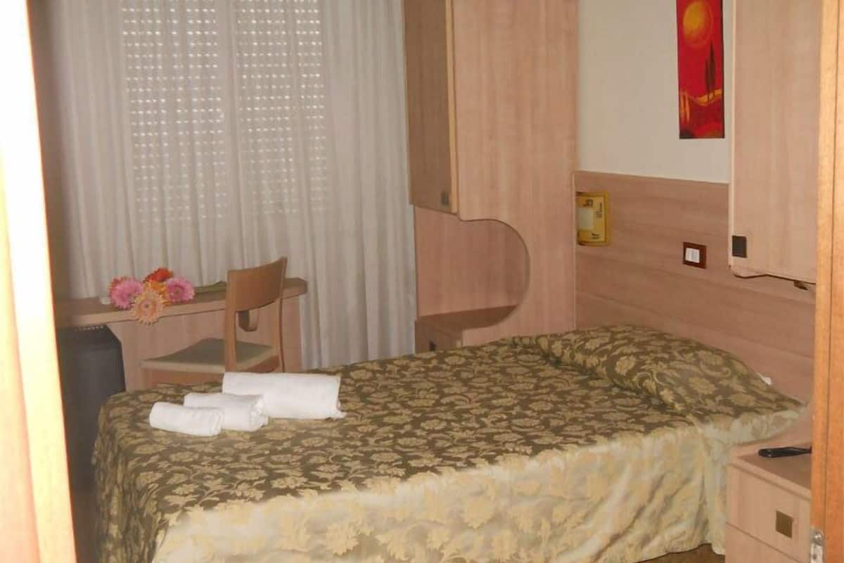 Habitación de hotel con cama, escritorio con silla, armario y un cuadro en la pared.