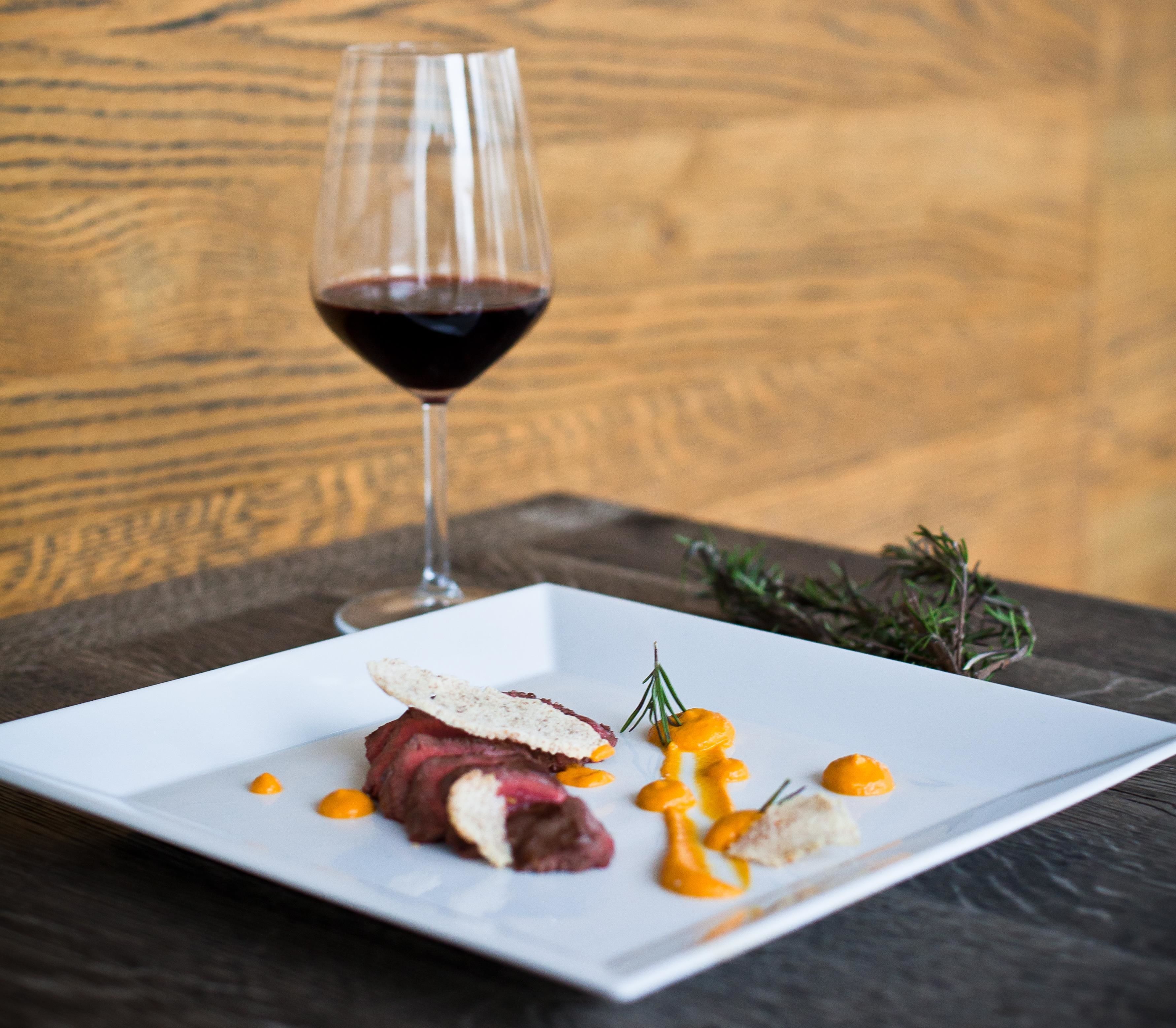 A white plate with a steak, sauce, and garnish on a dark wooden table.