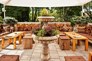 An outdoor seating area with wooden tables and benches, surrounded by lush greenery. - B&B Dvor Tacen (Ljubljana)