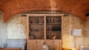 Una habitación acogedora con techo de ladrillo, un aparador de madera con botellas de vino, un sofá con cojines y una lámpara.