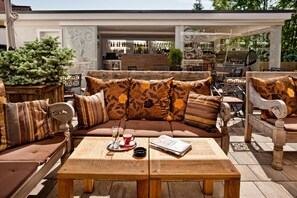 Un área de estar al aire libre con una mesa de madera, un sofá con cojines estampados y un árbol de Navidad.
