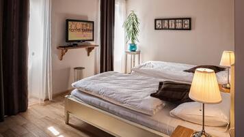 Un dormitorio ordenado con cama, lámparas de noche, televisor, planta y obra de arte en la pared.