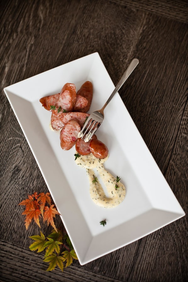 Un plato rectangular blanco con salchichas en rodajas y una salsa cremosa, sobre una superficie de madera oscura con hojas de otoño.