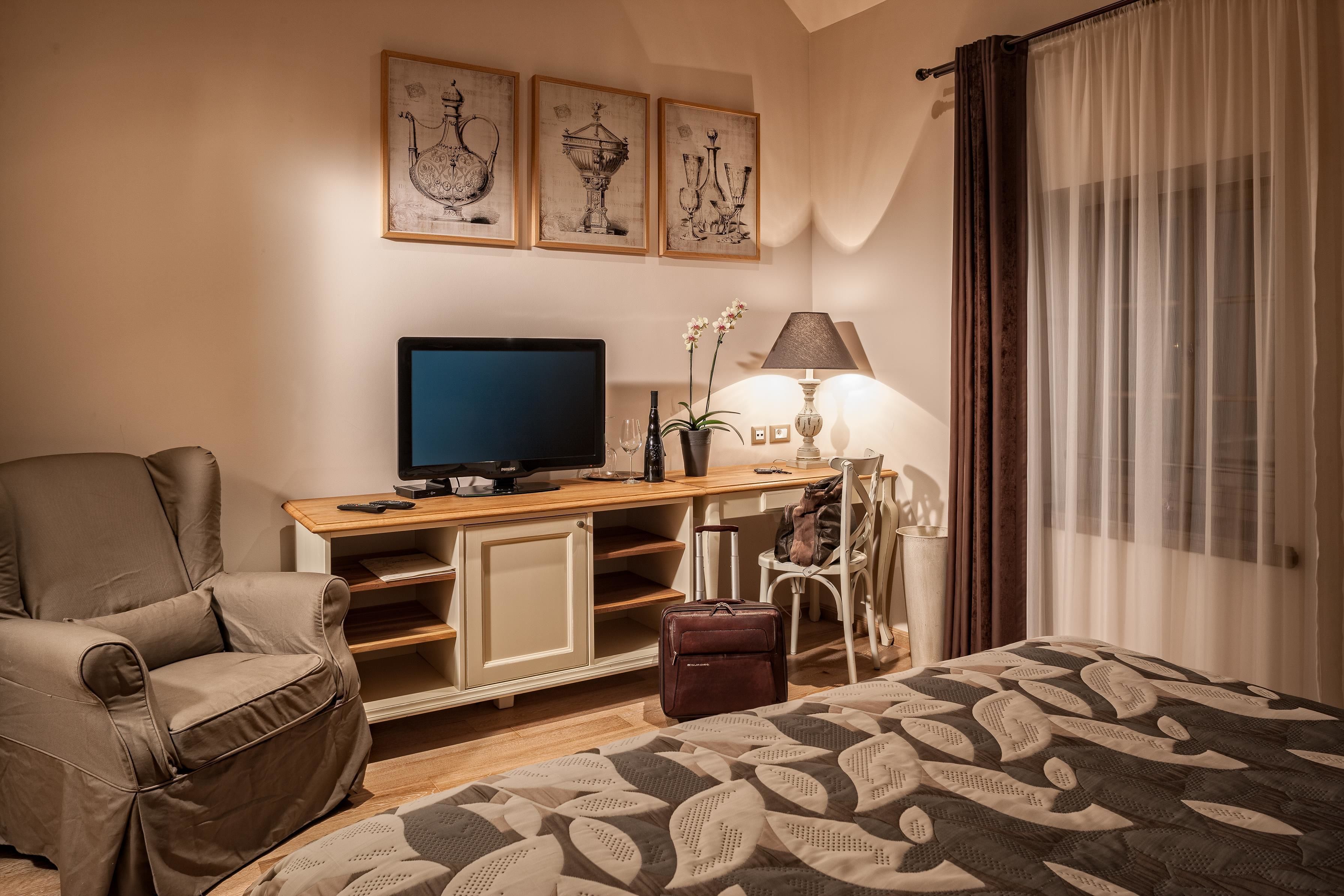A hotel room with a bed, a desk with a computer, a chair, a lamp, and artwork on the wall.