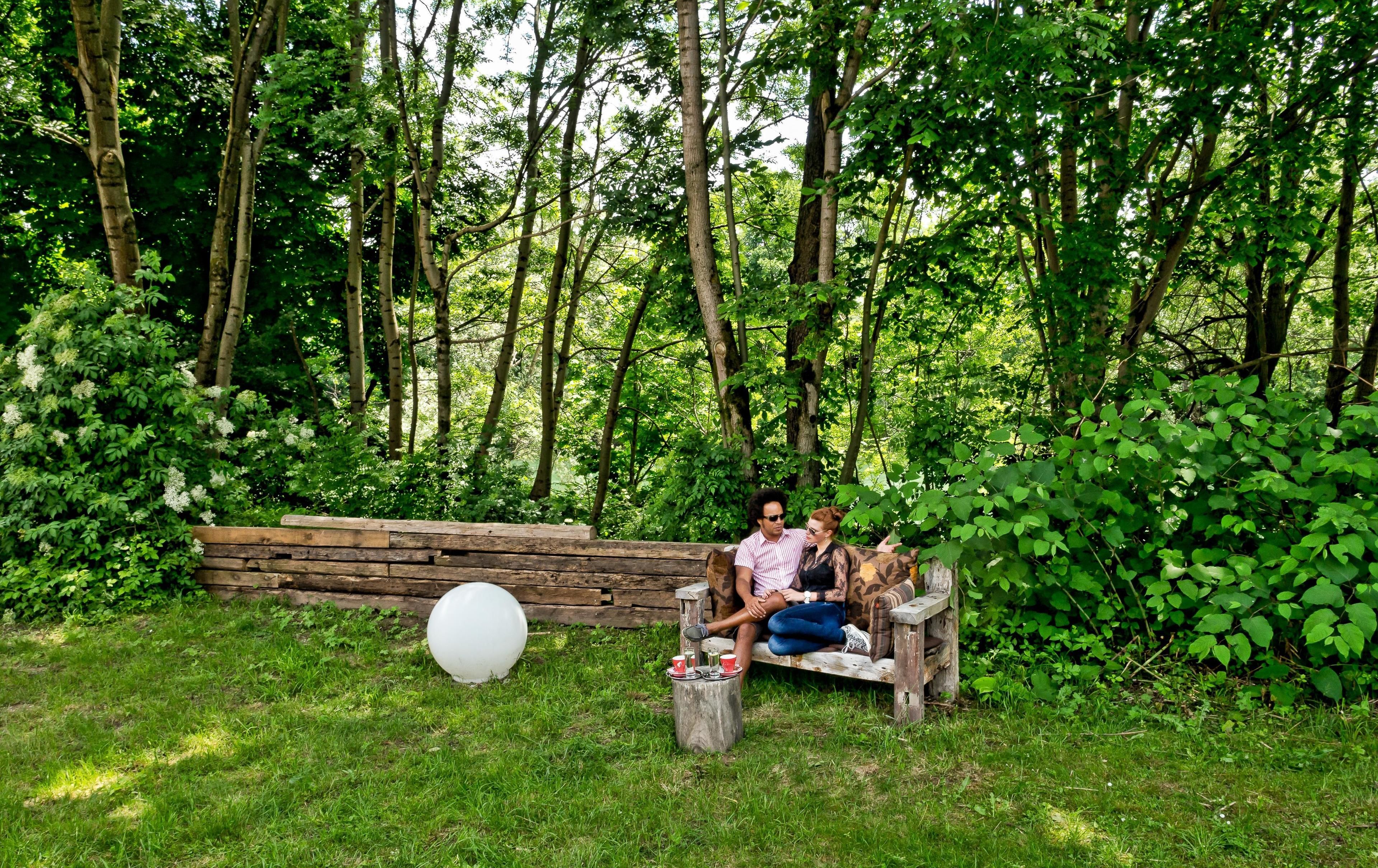 A wooden bench in a lush green garden with a white spherical object and a small table with cups.