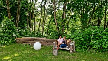 A wooden bench in a lush green garden with a white spherical object and a small table with cups.