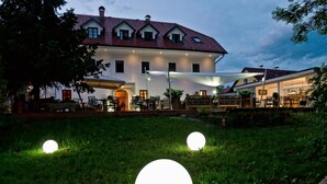 Un edificio con fachada blanca y techo rojo, zona de estar al aire libre con mesas y sillas, y dos esferas iluminadas sobre el césped.