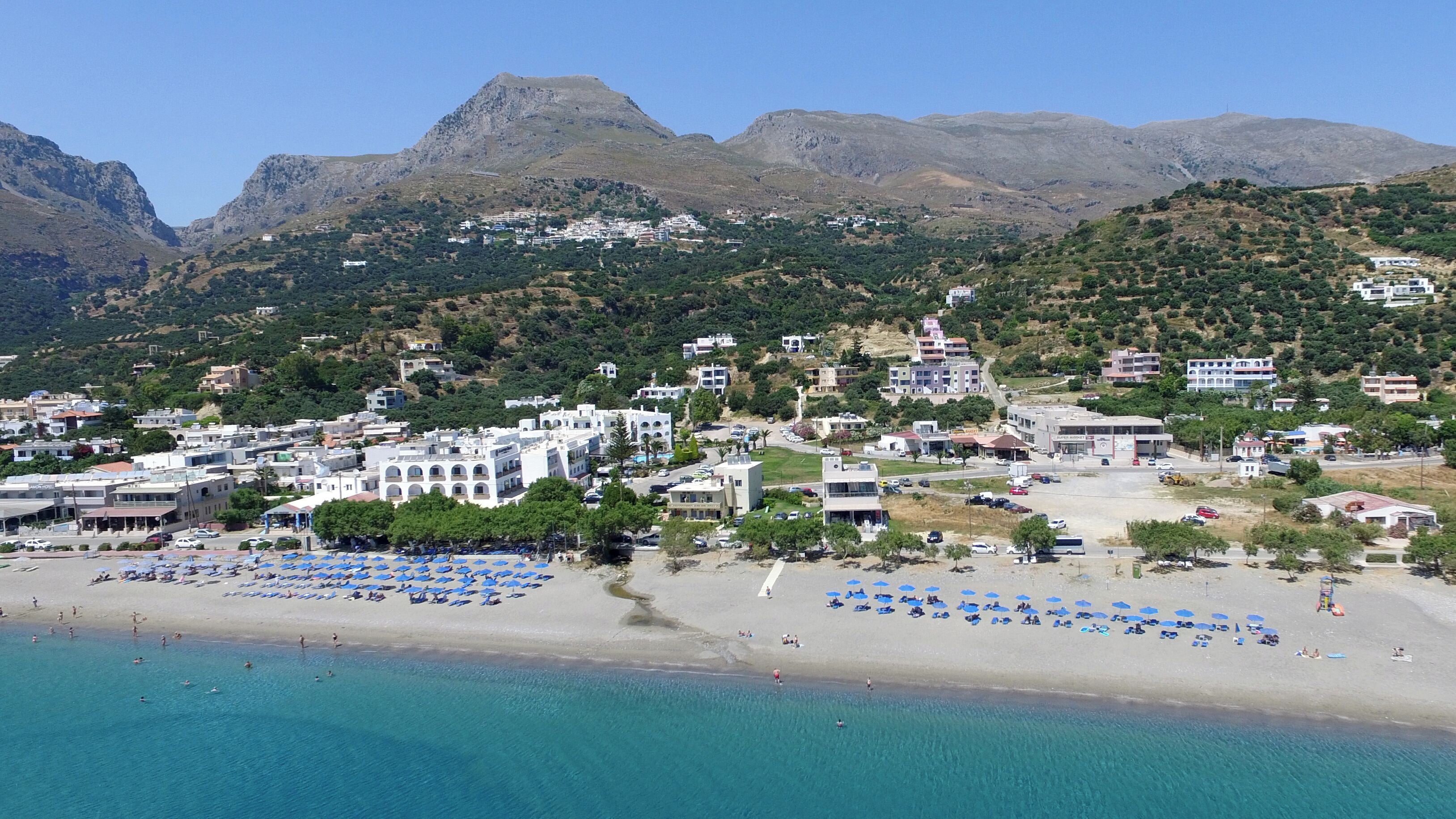 A coastal town with a beach, buildings, and mountains in the background.