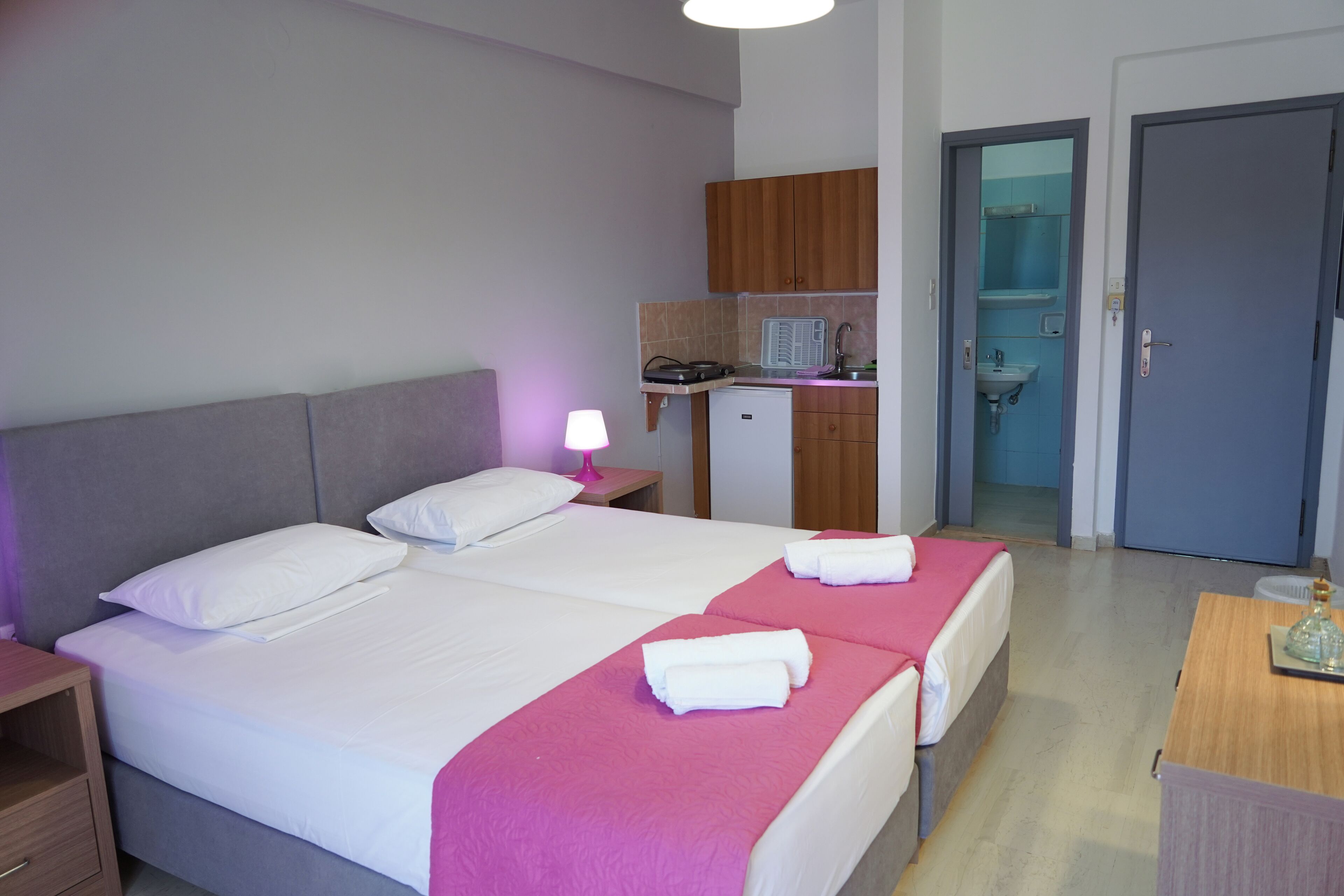 Ett hotellrum med två sängar, ett litet pentry och ett badrum som syns genom en öppen dörr.