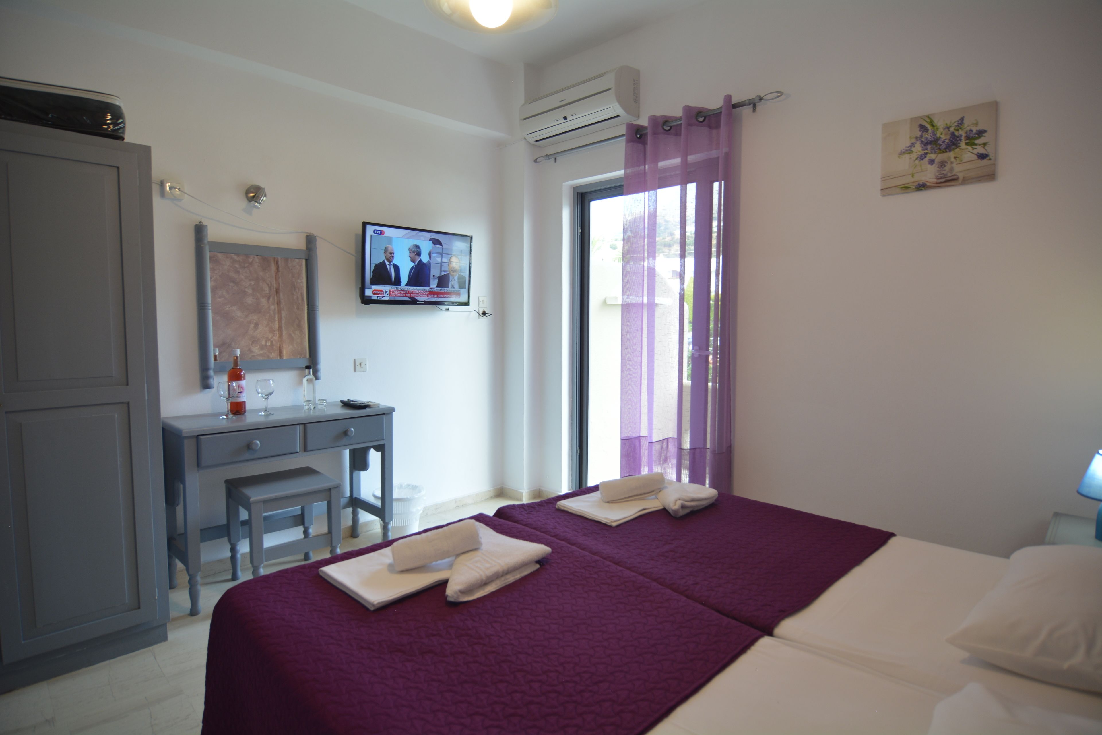 Habitación de hotel con cama, escritorio, silla, televisor y ventana con cortinas.