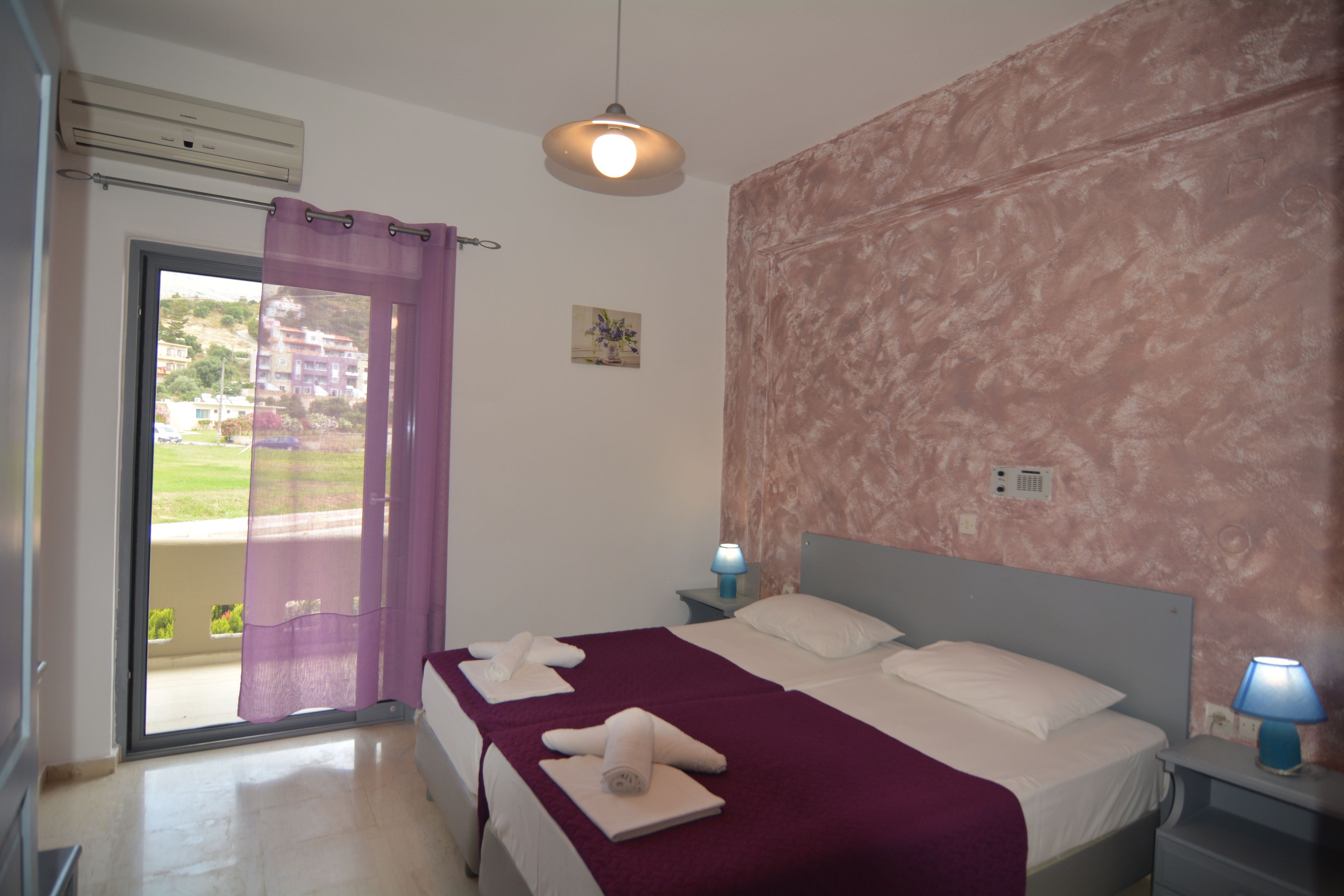 A bedroom with a bed, a nightstand, a lamp, a window with a view, and a door with a curtain.