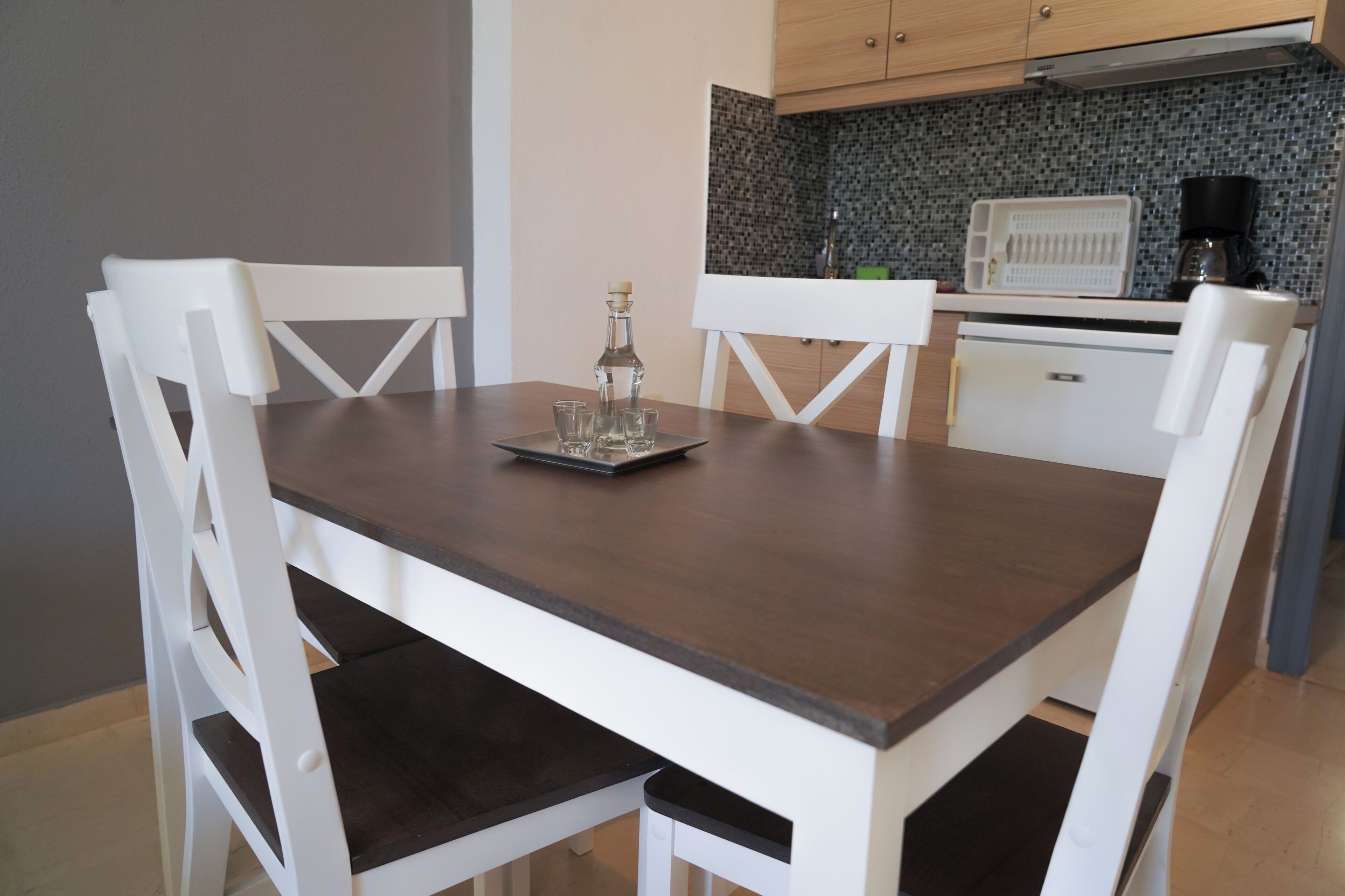 A dining table with chairs, a kitchen area with cabinets and a countertop, and a coffee maker.