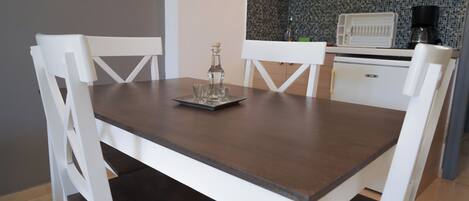 Una mesa de comedor con sillas, una zona de cocina con armarios y encimera, y una cafetera.