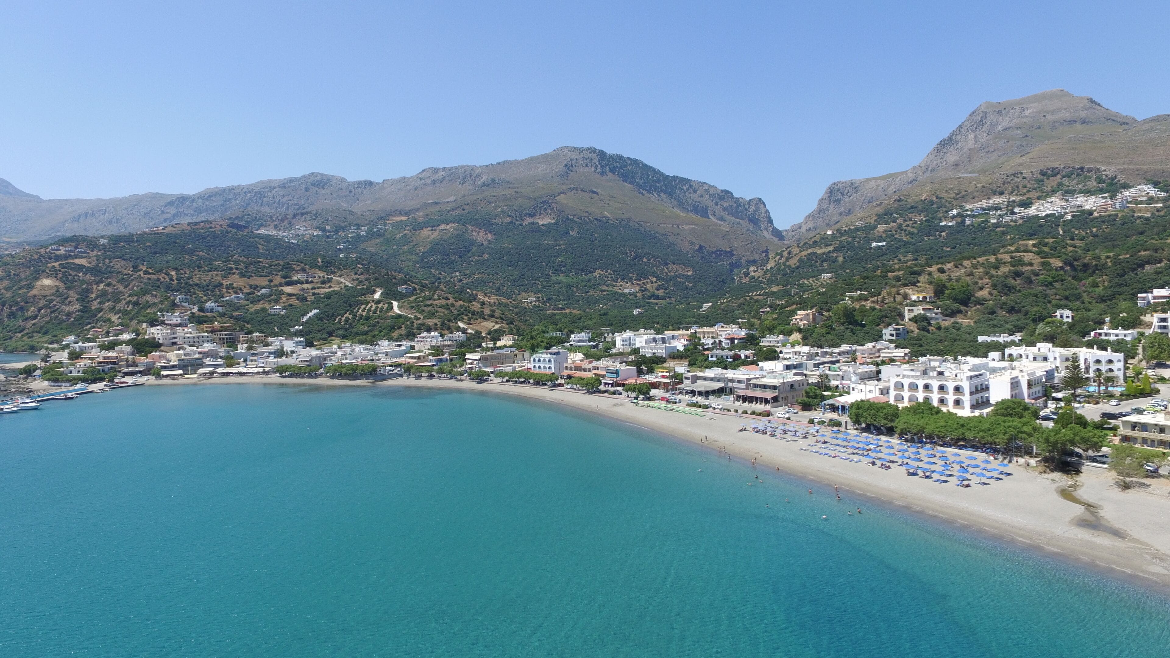 A coastal town with a beach, buildings, and mountains in the background.