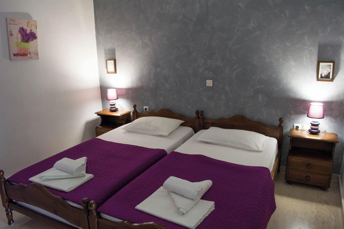 Una cama doble con una colcha morada, dos mesitas de noche con lámparas y una pared con un cuadro enmarcado.