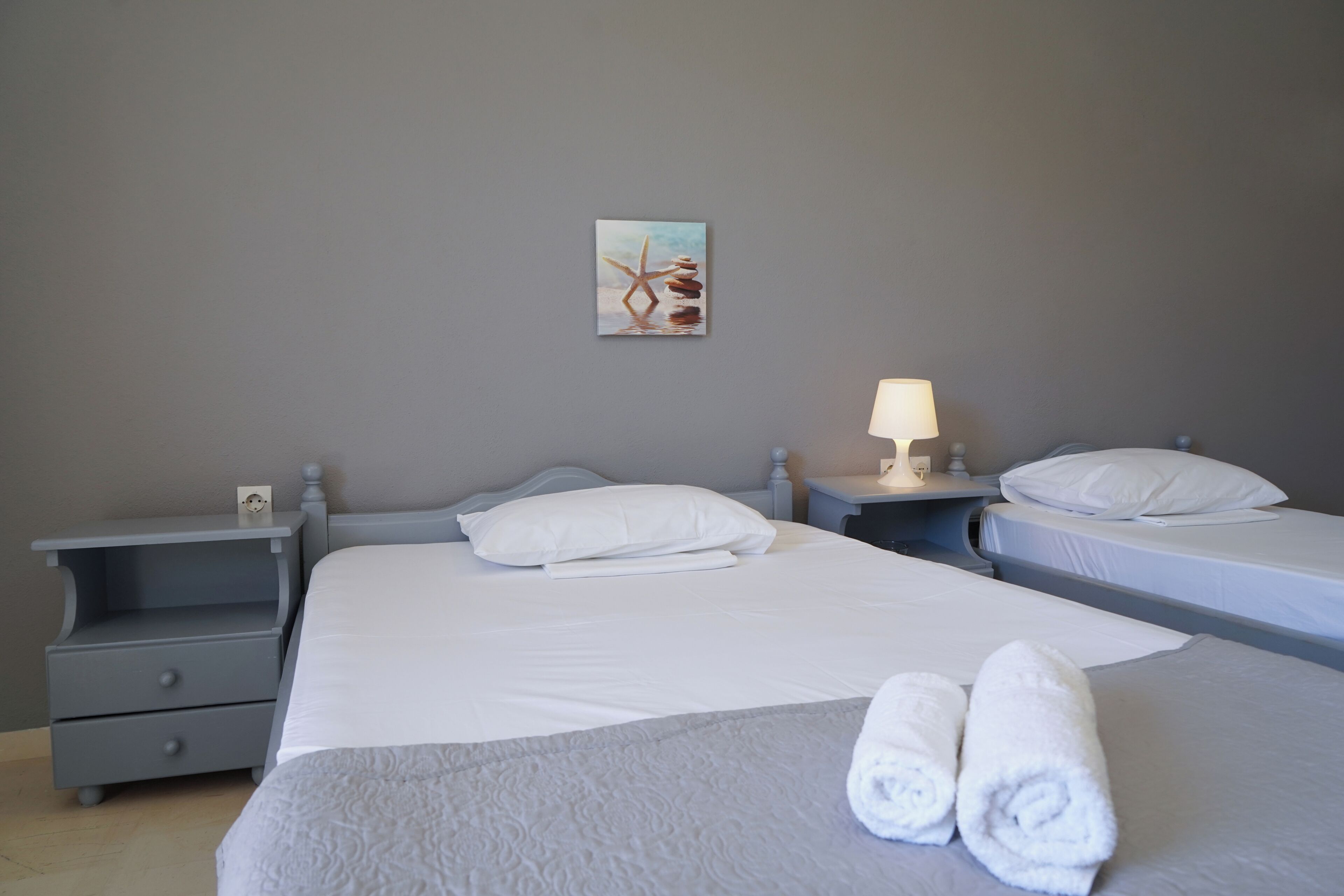 Ett hotellrum med en säng, två sängbord, ett litet bord, en lampa och en tavla på väggen.
