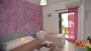 A hotel room with two beds, a balcony with pink curtains, and a table with fruit and a bottle. - Galini Beach (Agios Vasileios)