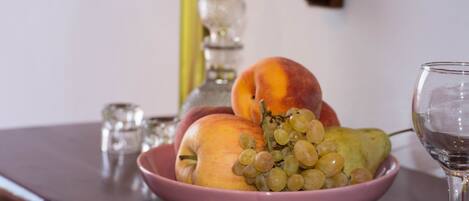 A pink bowl containing peaches, grapes, and a pear on a wooden table.