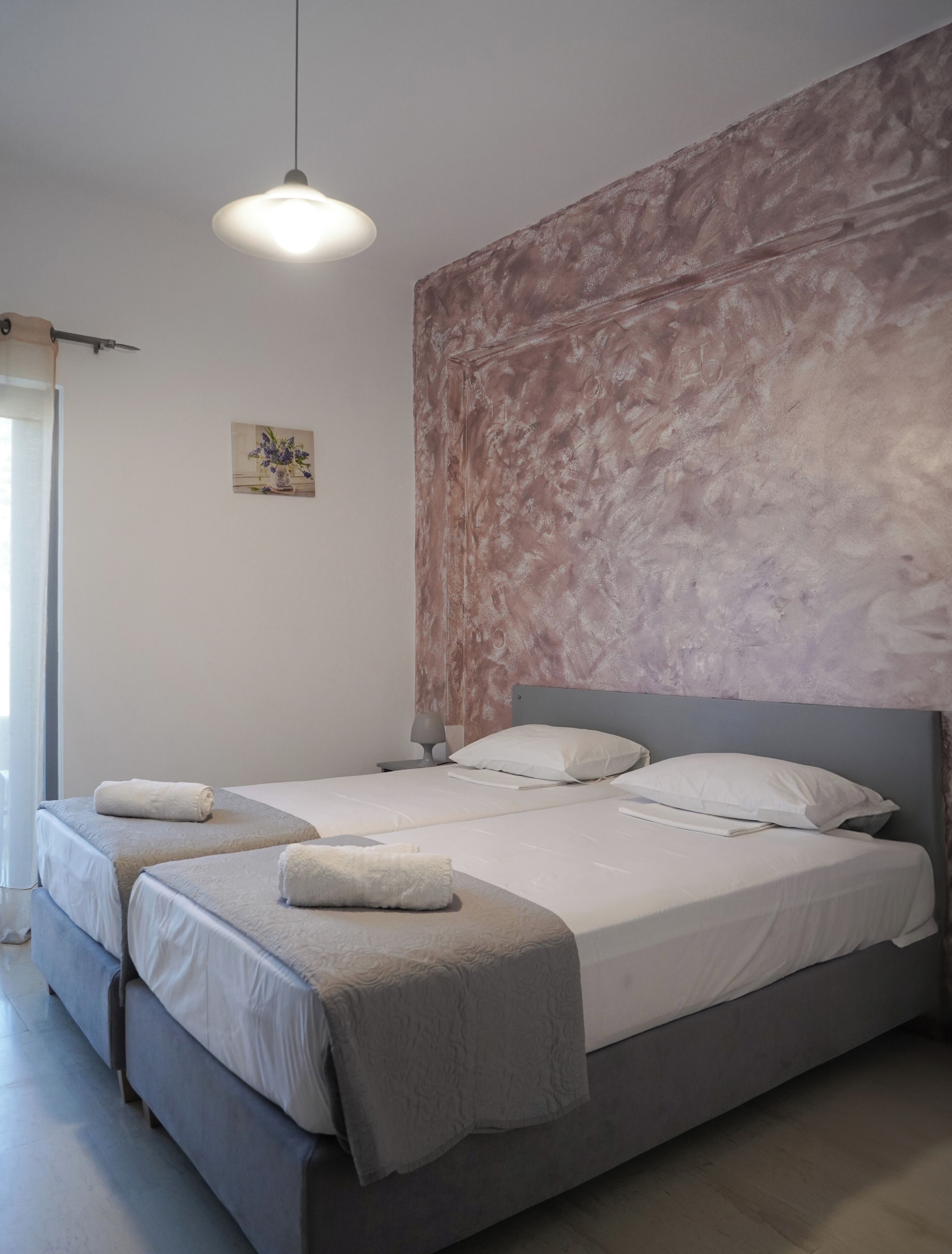 A double bed with a grey headboard and a textured wall behind it. There are two bedside tables with lamps, and a small painting on the wall.