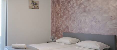 A double bed with a grey headboard and a textured wall behind it. There are two bedside tables with lamps, and a small painting on the wall.