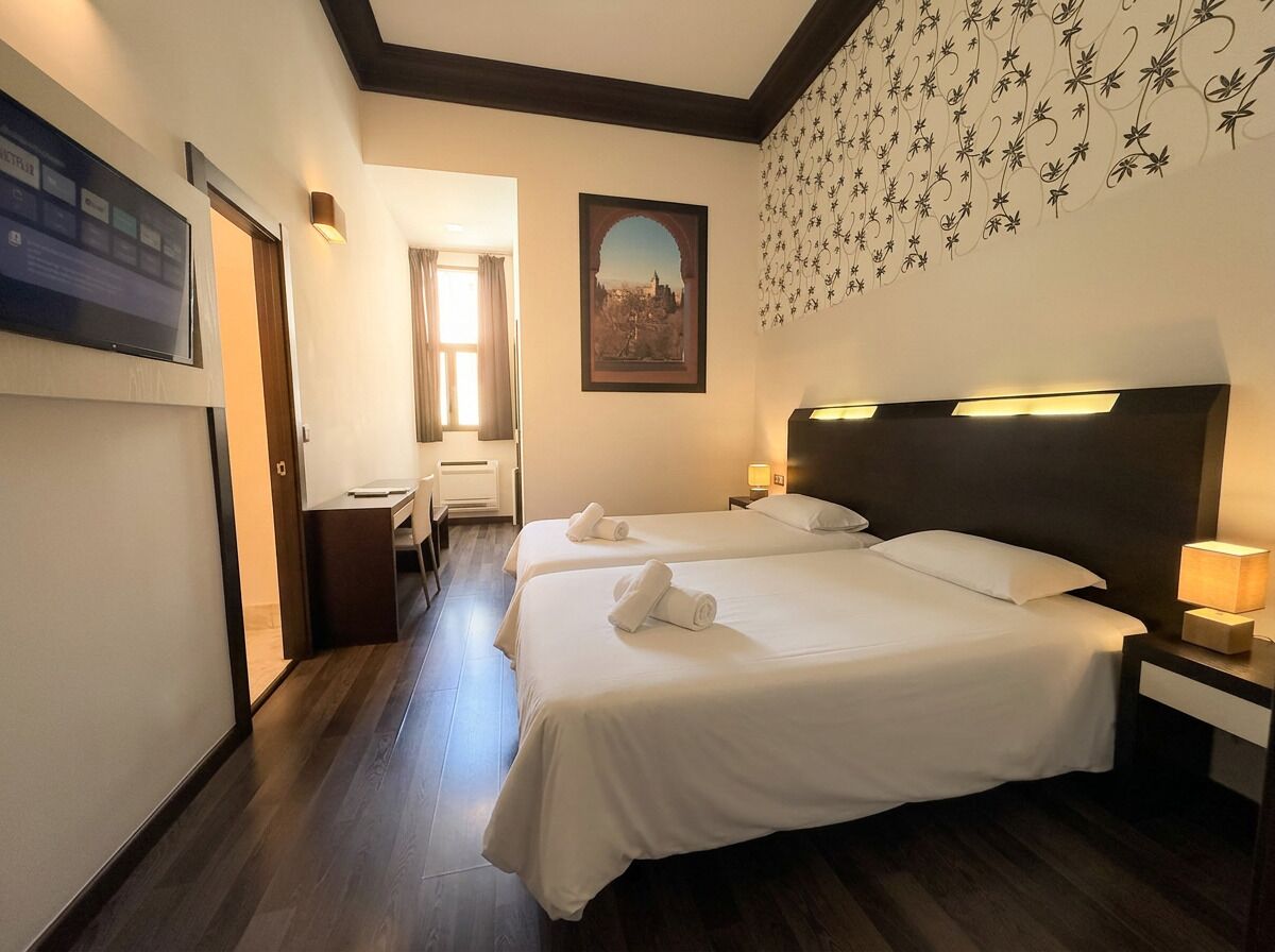 A hotel room with two beds, a TV, a painting, and a floral wall design.