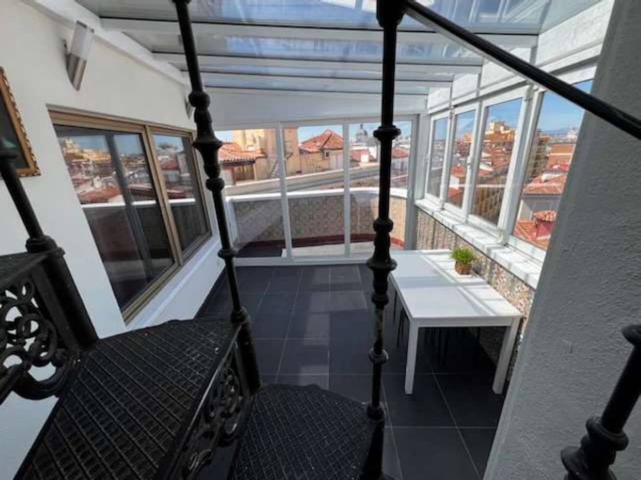 A covered balcony with a view of the cityscape, a small table, and a chair.
