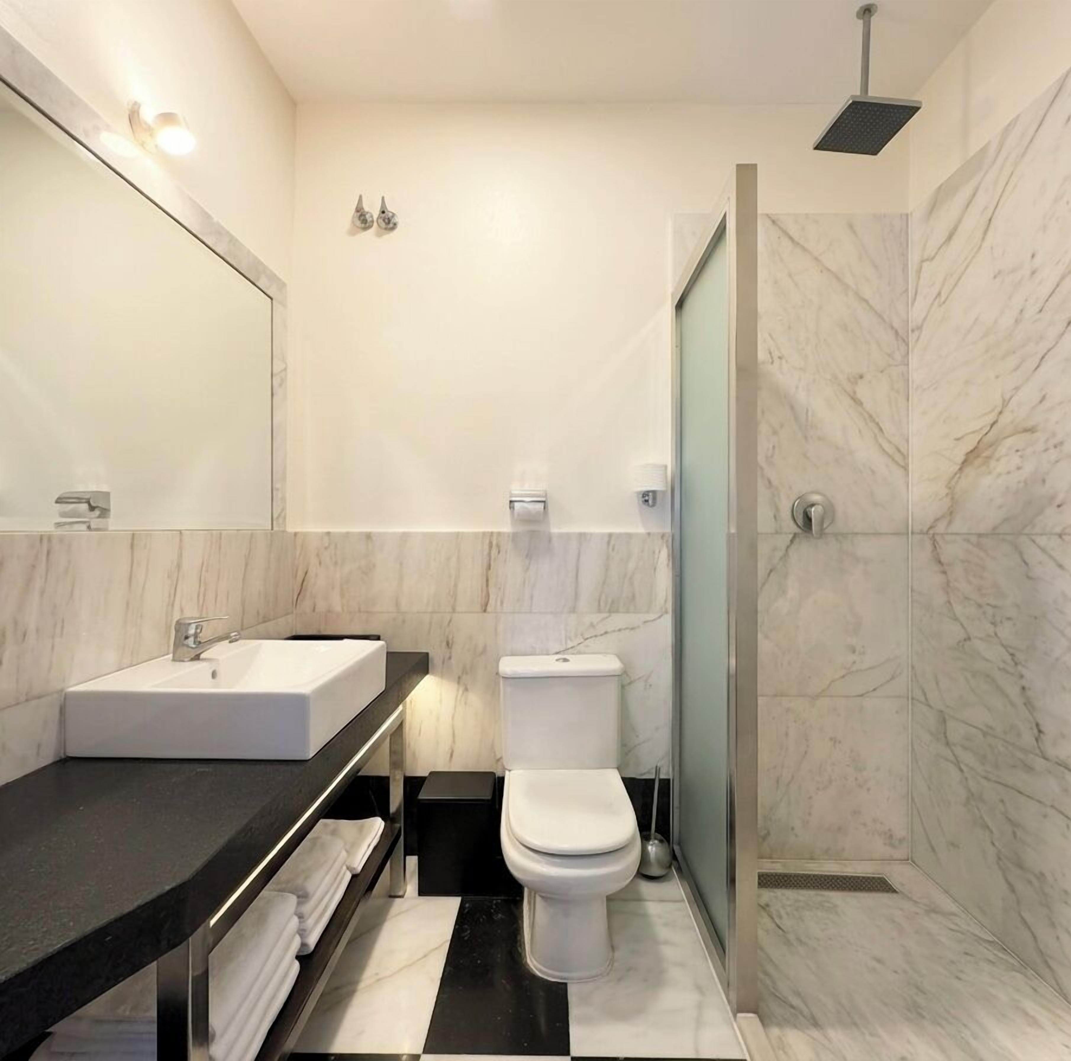 A modern bathroom with a marble floor, a white sink, a toilet, and a shower.