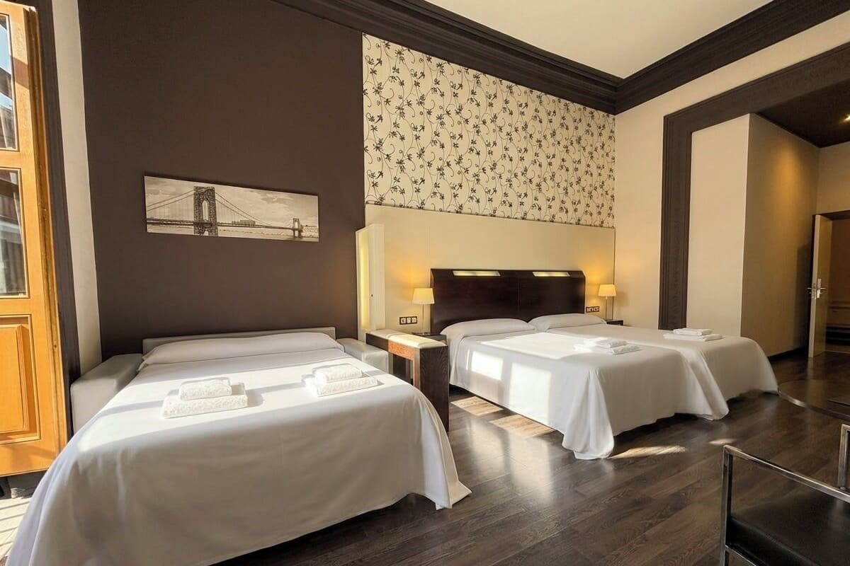 Habitación de hotel con tres camas, un ventanal grande y una obra de arte colgada en la pared.